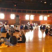Students seated in groups inside a sunlit dance studio 